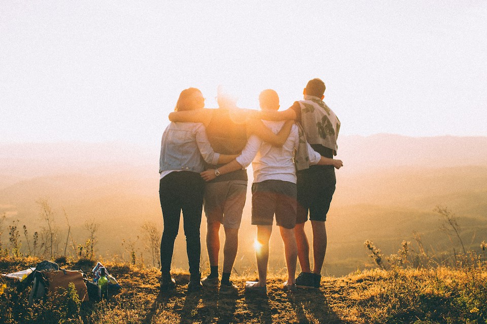 Group of people looking at sunset and embracing.