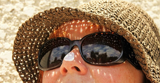 Person wearing hat, sunglasses and sunscreen on nose.